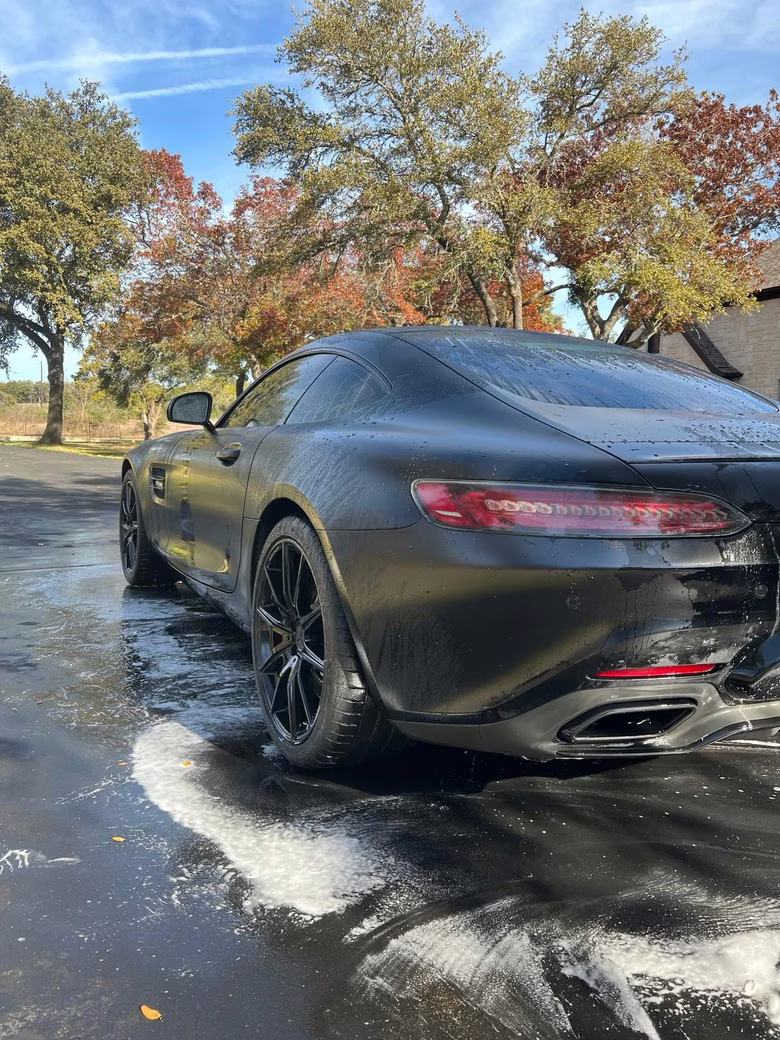 Black Mercedes-AMG GT covered in wash foam during a mobile detail on a tree-lined street